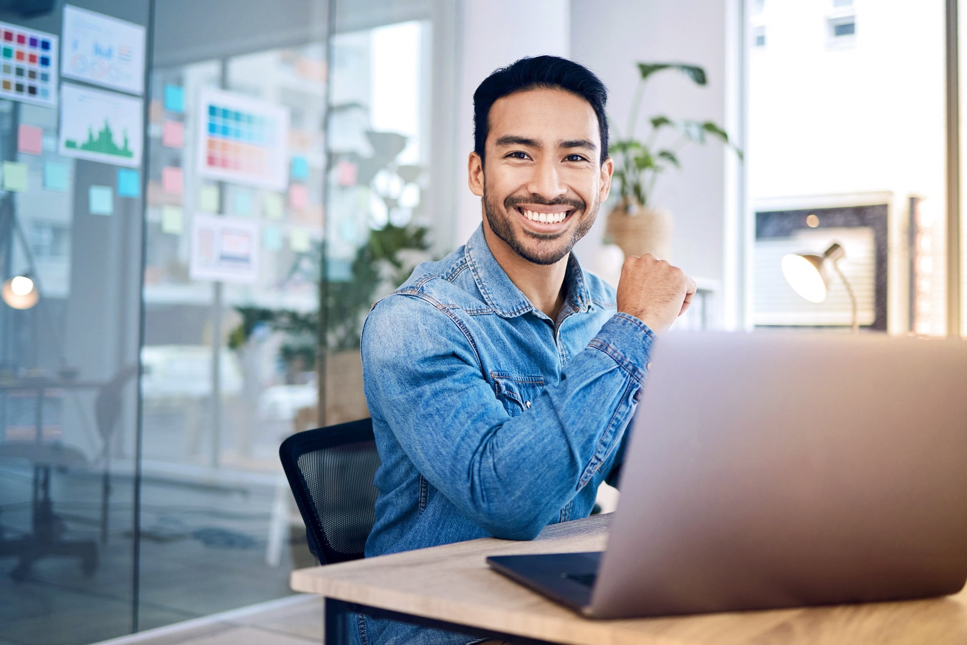 Ein lächelnder Mann vor einem Laptop im Büro