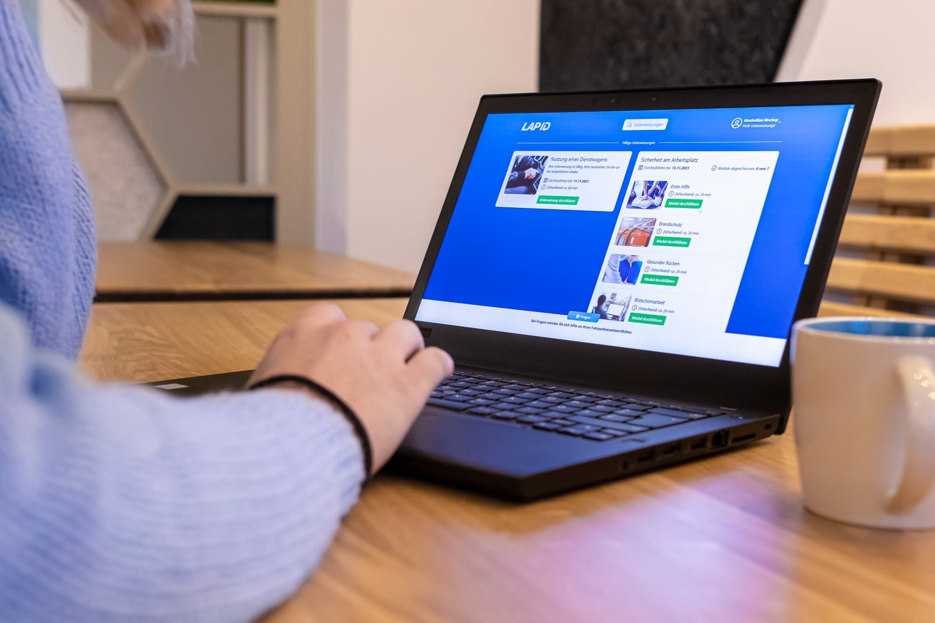 Modulkatalog von LearnID mit Mitarbeiterportal auf einem Laptop in einem Büro.